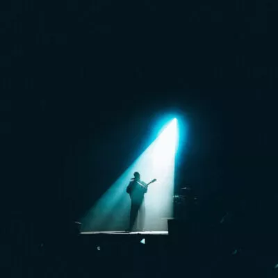 Homem tocando em concerto com facho de luz o iluminando.