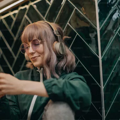 Mulher jovem usando fone de ouvido com celular na mão.